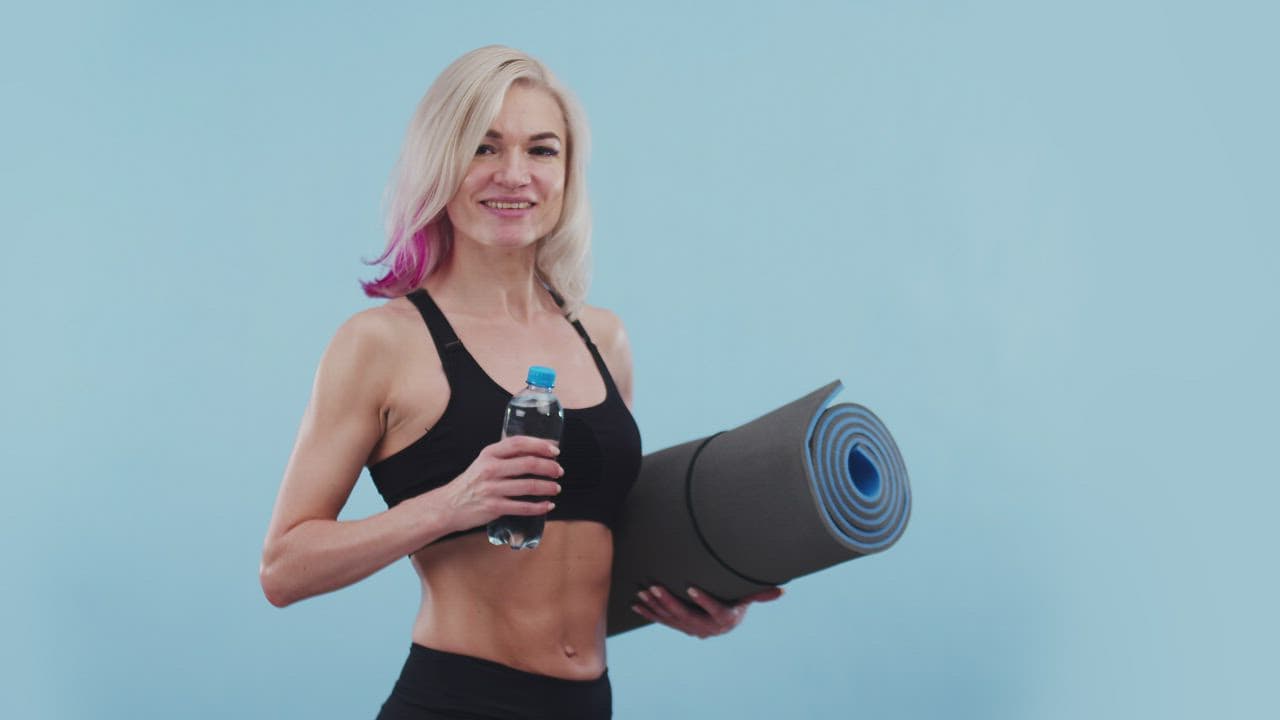 Smiling fit woman holding a yoga mat and a water bottle